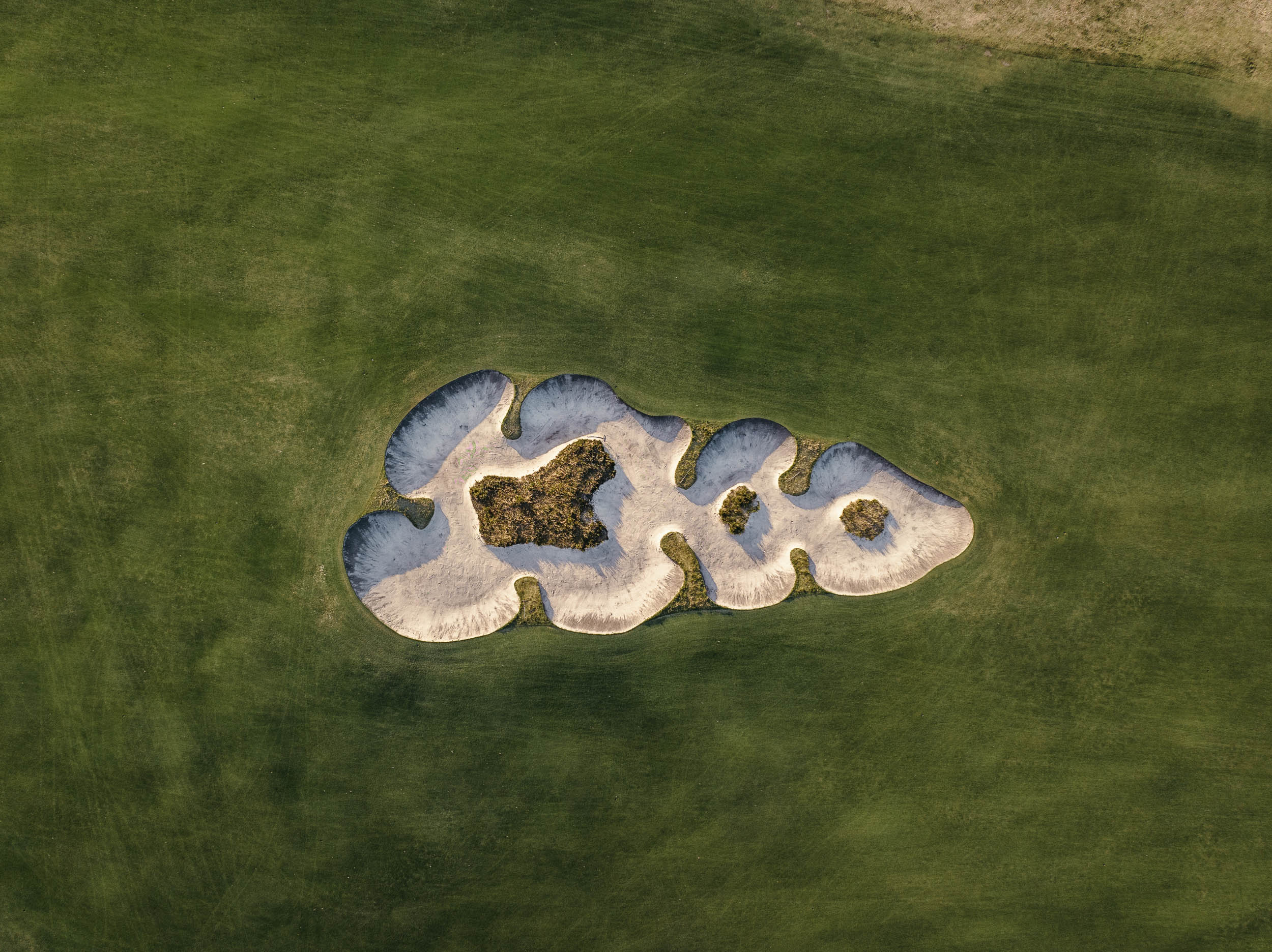 A Royal Melbourne bunker seen from directly above, its lips ragged against the fairway